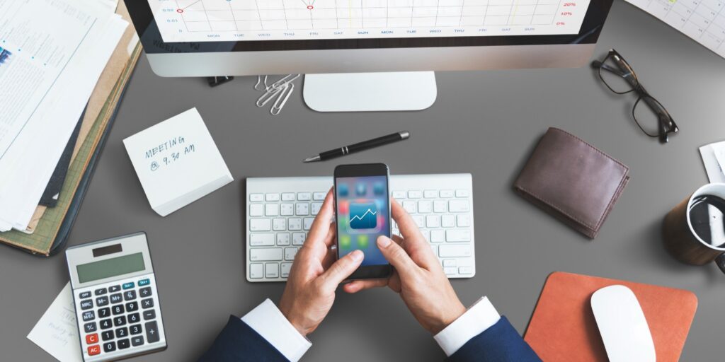 Business man sat at desk working from mobile phone, with keyboard, calculator, workpad on desk.