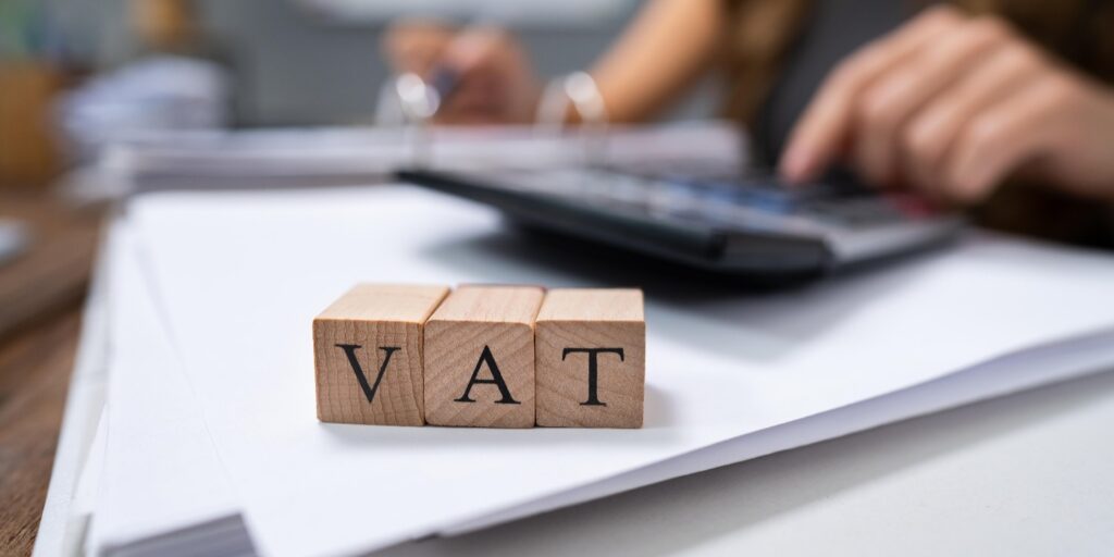 Person working on VAT calculations for their business at a desk, with VAT wooden blocks at the front.