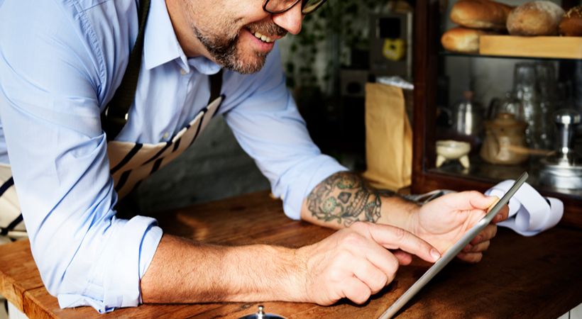 Man checking finances in hospitality bar area using tablet.