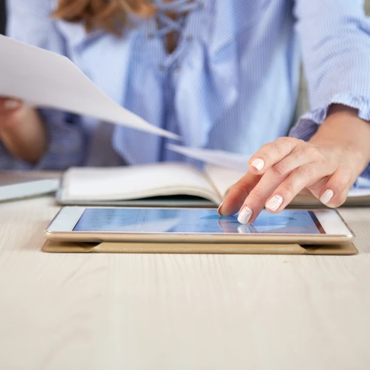 Business professional analysing data charts on a tablet while reviewing paperwork at an office desk